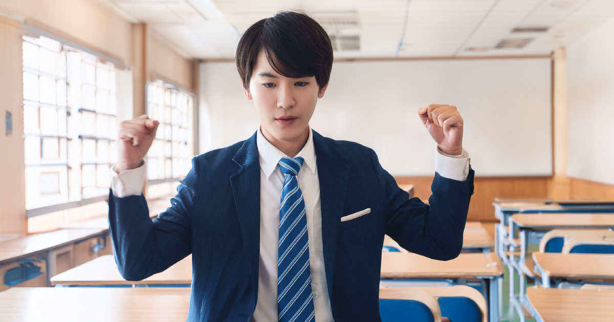スーツ姿で教室に立つ人物、両手を挙げガッツポーズ
